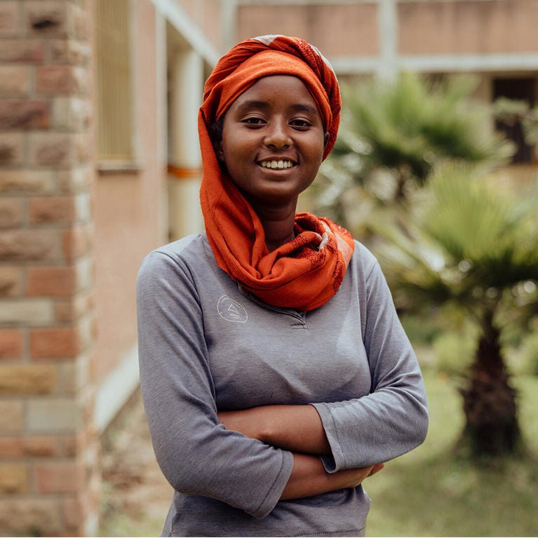 Azeb, a girl wearing a red head wrap, stands with her arms crossed. With the help of World Vision, she now advocates for children’s rights and gender equality in her community.