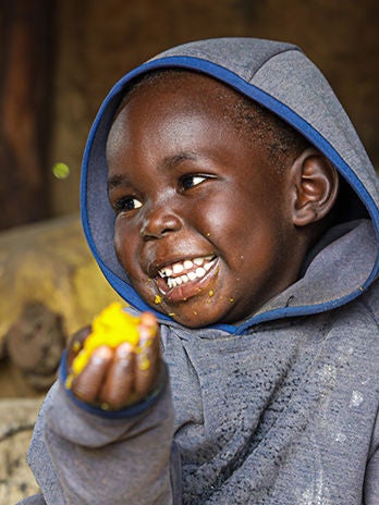 A child wearing a grey hooded jacket is enjoying nutritious food.