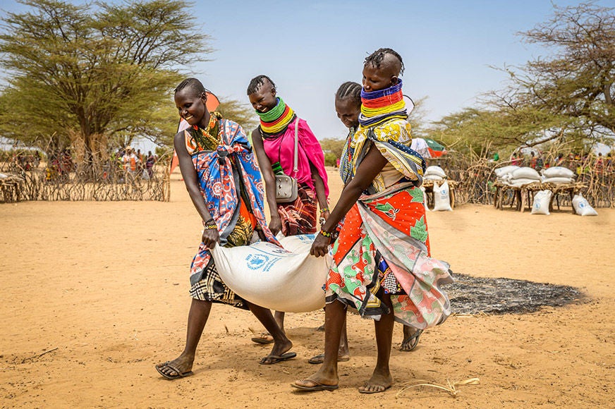 Four women return home with a 50kg sack of sorghum food ration at a World Vision distribution in Nakorio village. (Kenya, 2022)