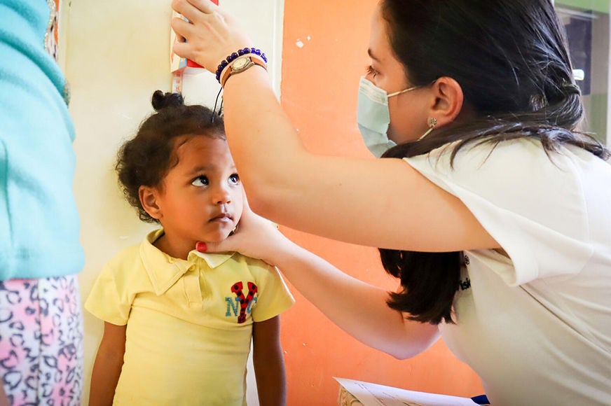 A World Vision staff member is taking the height measurement of a child.