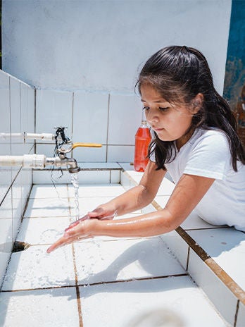 A young girl washes her hands outside of the new latrines supplied by World Vision at a school in Copan Ruinas. (Honduras, 2023)