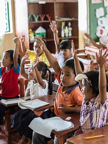 A group of children, raising their hands high, actively participating in a classroom.