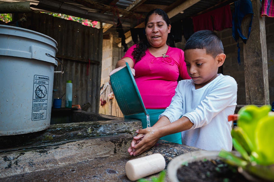 A mother pours water on her son’s hands after receiving new latrines and access to clean water through World Vision child sponsorship in Copan Ruinas. (Honduras, 2023)