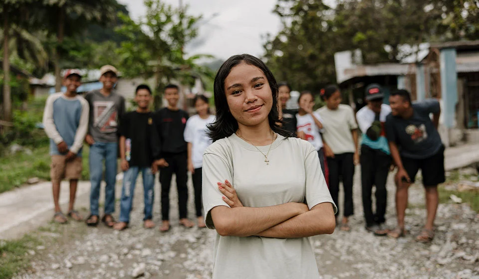 A girl in a white shirt, crosses her arms and smiles. (Indonesia, 2023)