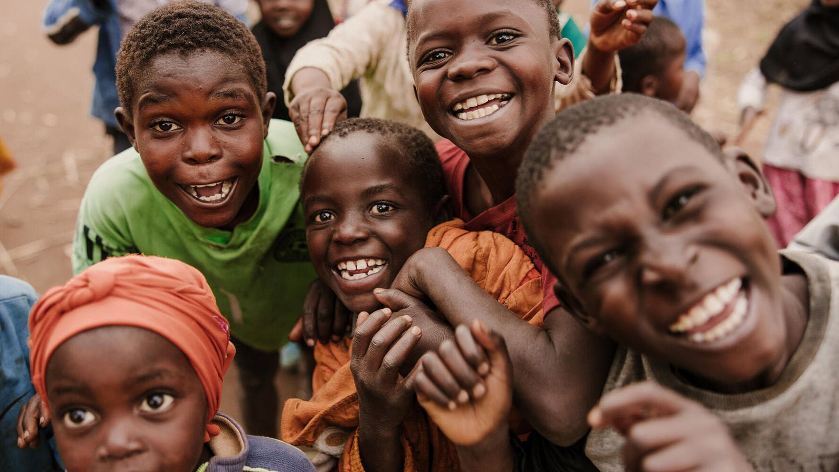 A group of children gather, smiling and laughing. 