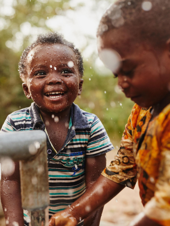 Chiild smiling next to a water pump.