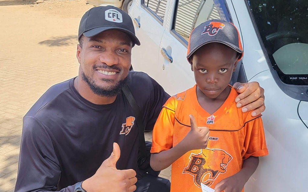 Boseko Lokombo and young boy give a thumbs up in BC Lions shirts and caps. (Kenya, 2024)