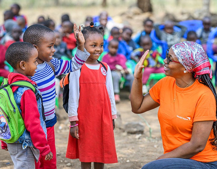 World Vision staff, Esther, high-fives three children at a school in Mbuyani village. (Tanzania, 2023)