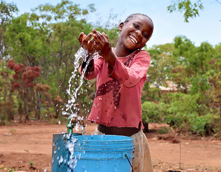 A girl wearing a red blouse is playing with the water she collected from the tap.