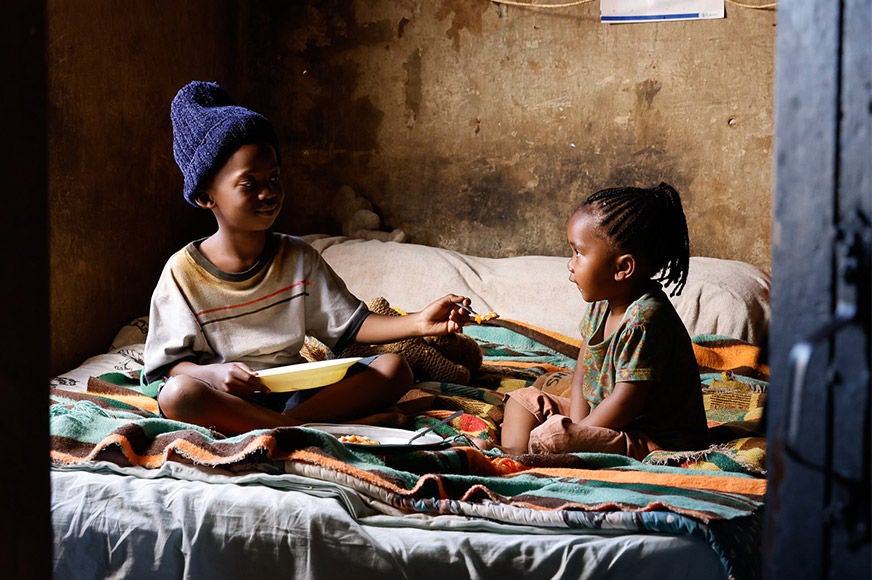 A boy sitting on a bed, sharing his food with his younger sister.