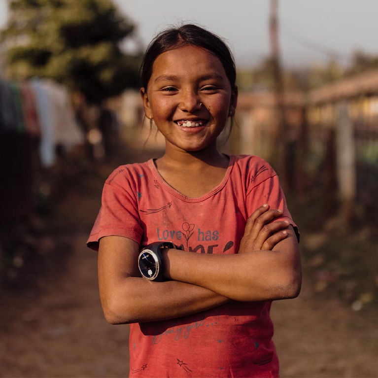 Sapuna, arms crossed, smiled at the camera. Children in her community face significant challenges in terms of education, child protection, livelihood, and health.