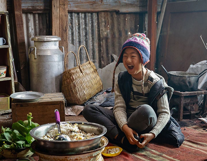 A boy wearing a knitted hat is sitting on the floor laughing.