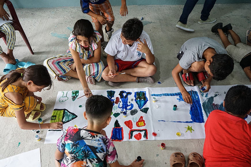 A group of children sit on the floor painting and drawing in San Pedro Sula, as part of an art therapy initiative in collaboration with the Honduras National Autonomous University. (Honduras, 2023)