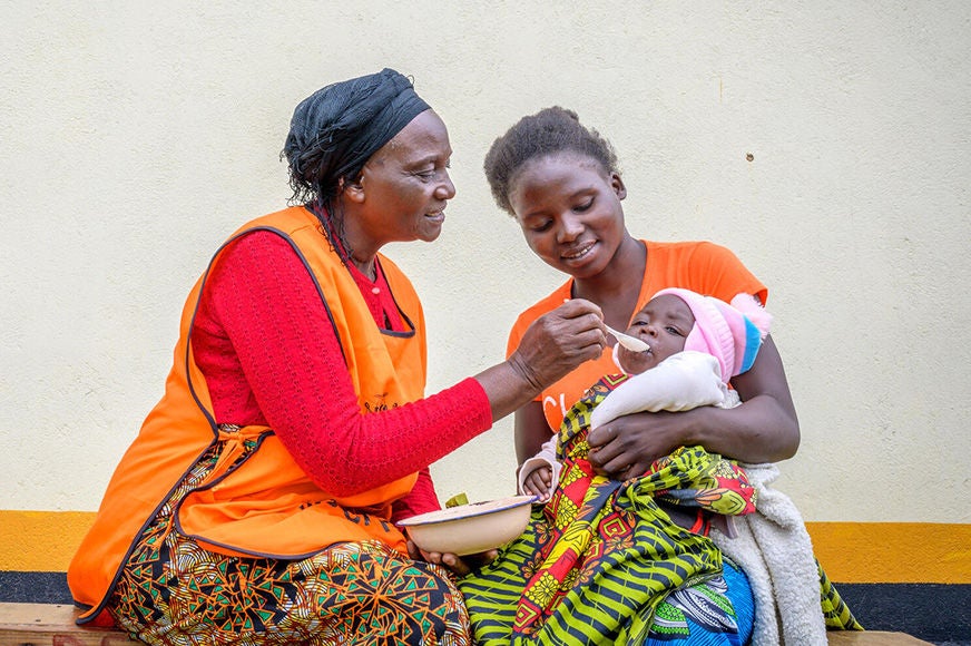 A mother holds her baby who is being fed by World Vision staff.