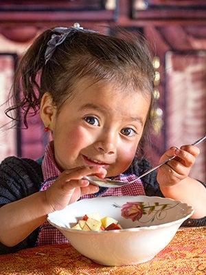 A girl holding a spoon enjoys her food inside her home.