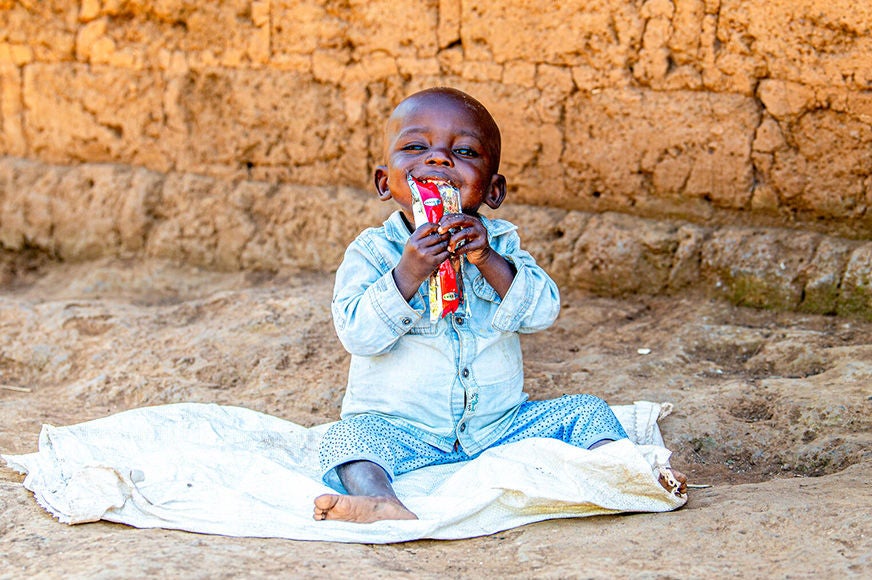 A small child is sitting, eating a packet of ready to use therapeutic food.