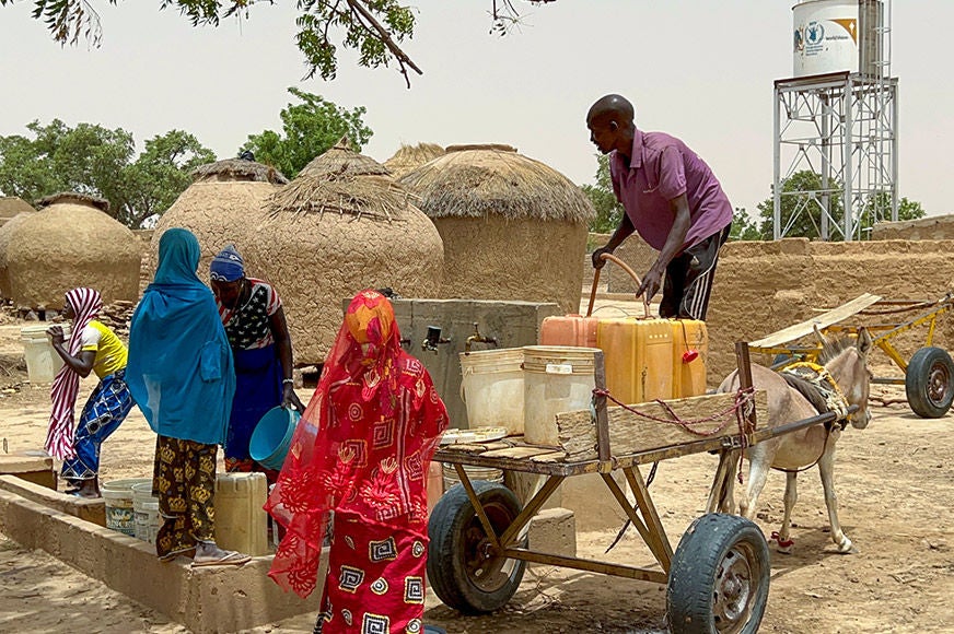 A group of people filling buckets with drinking water from a communal water source. (Niger, 2023)