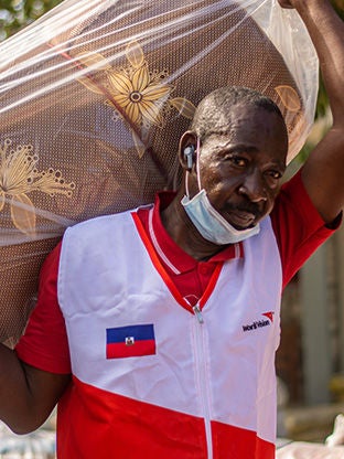 A World Vision staff is carrying a sleeping mat.