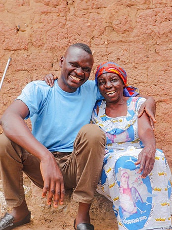 Matieu, a former World Vision sponsored child, sits outside of his childhood home, embracing his grandmother.  (Democratic Republic of the Congo, 2024)