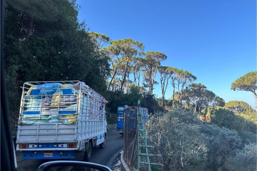 A large truck packed with pillows and blankets climbs a hill. Others are ahead of it. 