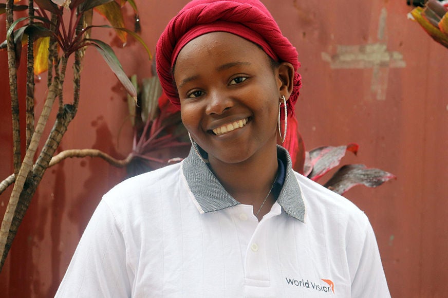 A World Vision staff member is smiling while she stands in front of a red wall. (Democratic Republic of Congo, 2023)