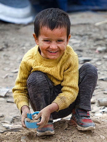 A smiling child is playing with his toy on the ground outdoors.