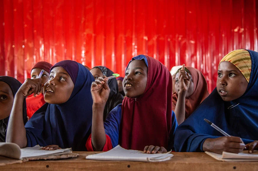 Three young girls listen to their teacher at an Internally Displaced Persons primary school in Dollow, Somalia. (Somalia, 2023)