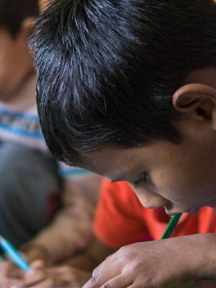 Child writing on desk at school.