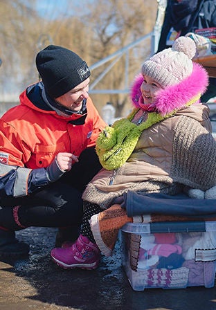 A World Vision staff is talking to a little girl sitting on a box of clothes at the Siret border in Romania.