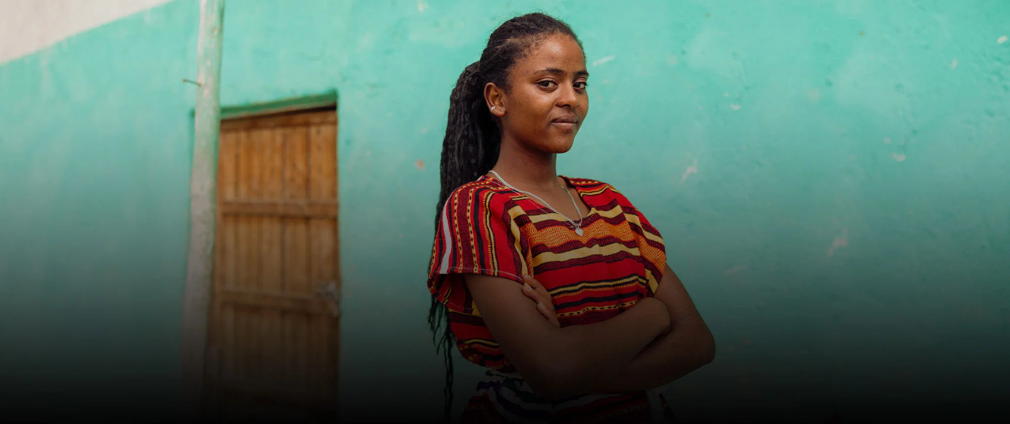 Young girl standing next to a wall with her arms crossed.