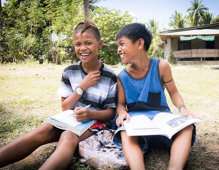 Two boys are sitting on the ground while holding a book.