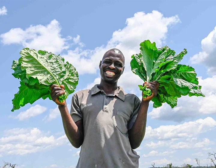 A man smiling and showing off the harvest of his garden.