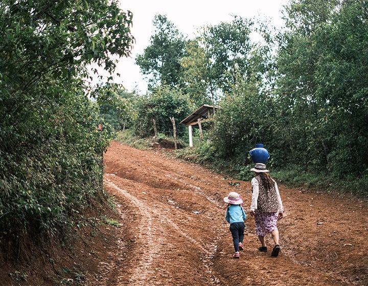 A woman carrying a jug of water on her head walks on a dirt road alongside a young girl. (Honduras, 2023)