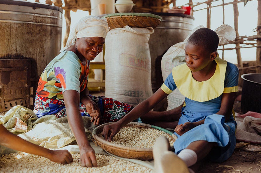 A student helps her teacher prepare lunch as part of their community’s school feeding program, implemented by World Vision. (Kenya 2023)