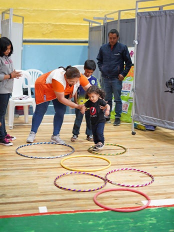 World Vision staff helps a small child jump through hula-hoops at a child friendly space.