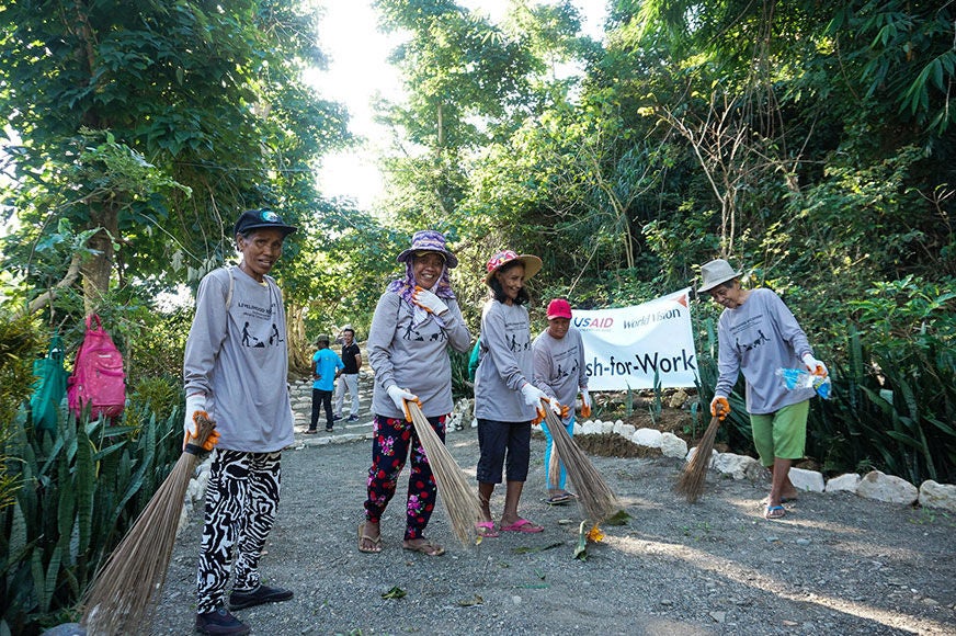 A group of women sweep the path leading to a tourist spot as part of a World Vision cash-for-work program, which supports typhoon-affected families. (Philippines, 2019) 