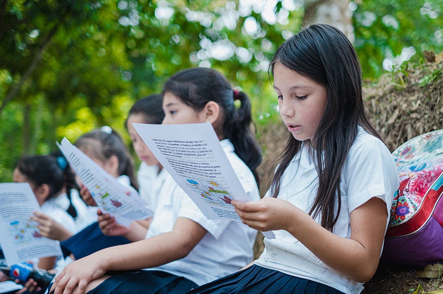 Sheril (right) reads outdoors with classmates at a reading camp in Mayo Area Program, in Copan Ruinas, Honduras. (Honduras, 2023)