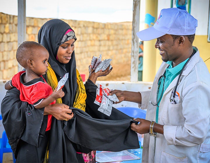 World Vision staff gives mother holding her child packages of ready-to-use therapeutic food at a nutrition center.