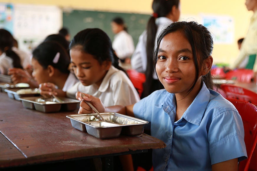 A young girl is eating a meal in school as part of a feeding program. (Cambodia, 2023).