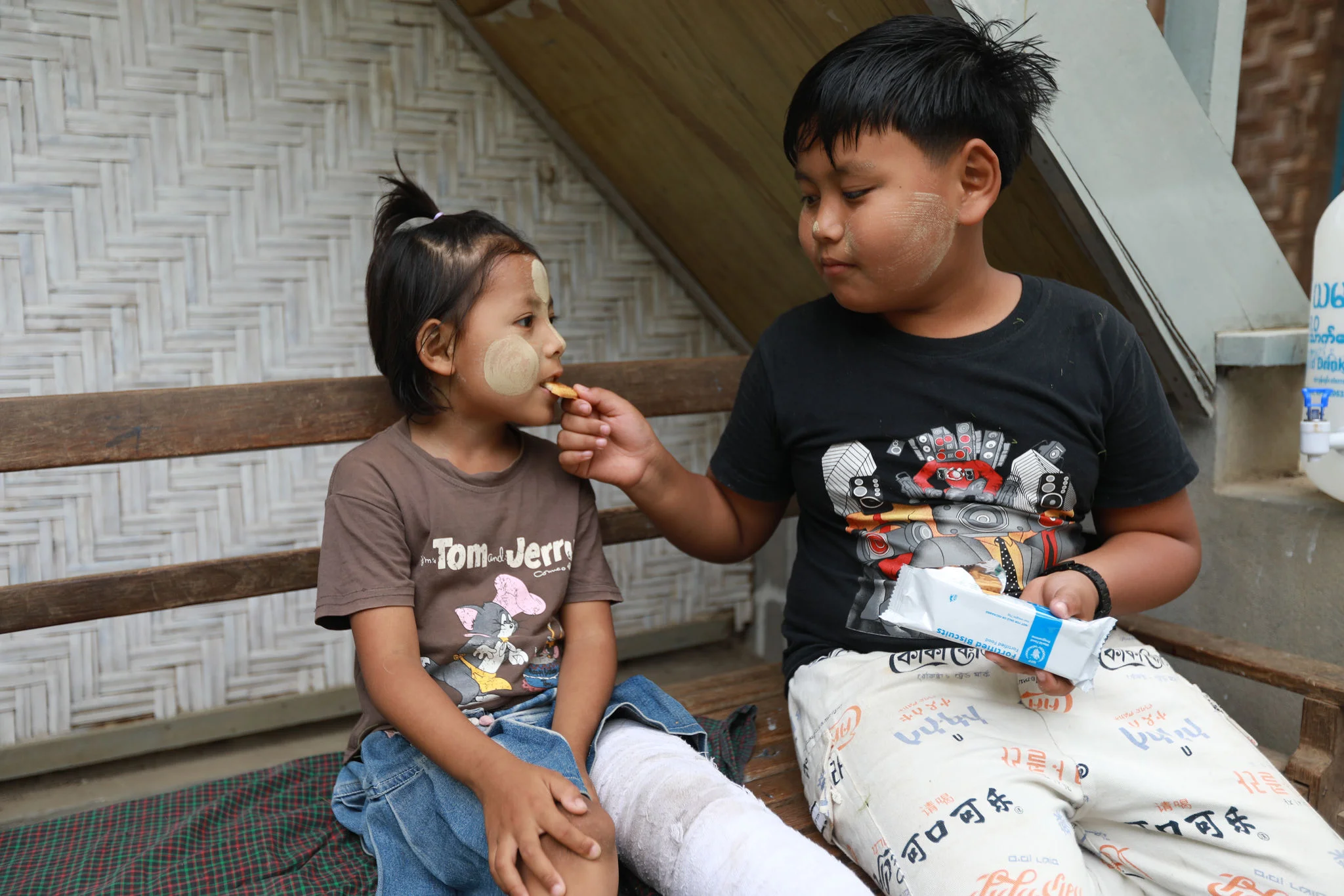 A young girl being fed by her brother.