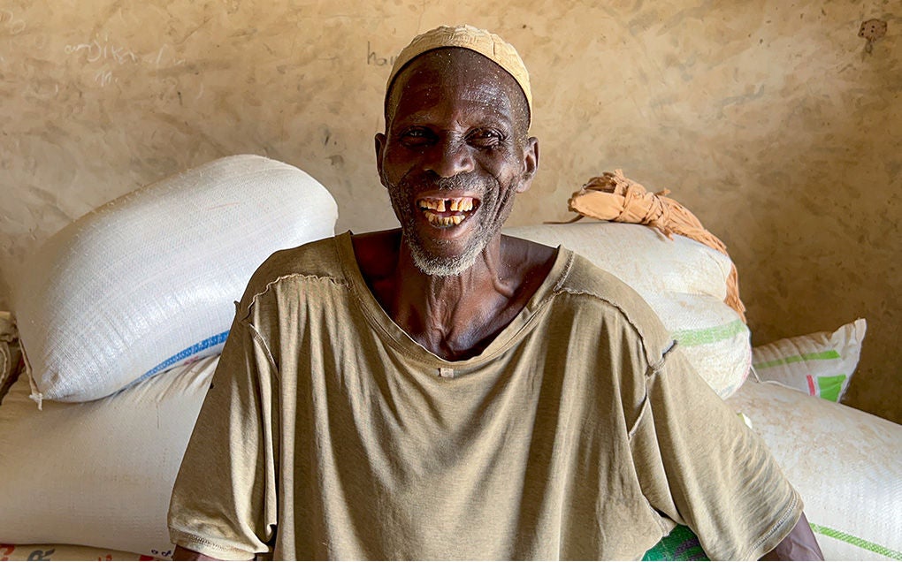 A man smiling in front of stacked bags of grains.