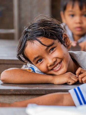 A smiling girl in school uniform is leaning on her desk.