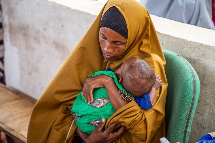 A woman holds her child at the Towfiiq Primary Healthcare Centre, a government-run clinic supported by World Vision. (Somalia, 2022)