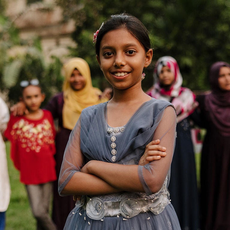  A girl wearing a blue dress, standing with arms crossed. World Vision’s child protection training helped children in Barishal area program.