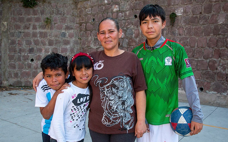 Mother Rosa stands with her three children in front of a stone wall. (Ecuador, 2022)