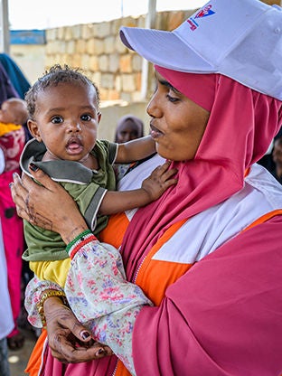 A World Vision staff is carrying a child outside a health center in Somalia.