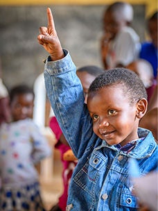 A young boy raising his hand in a classroom.