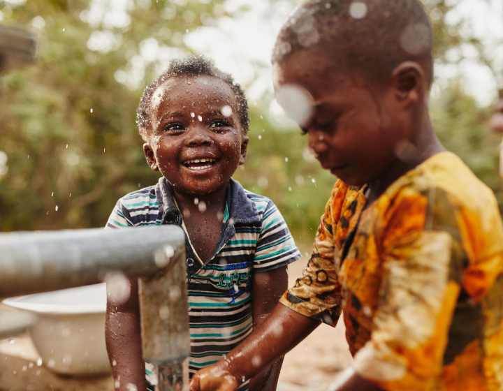 Chiild smiling next to a water pump.